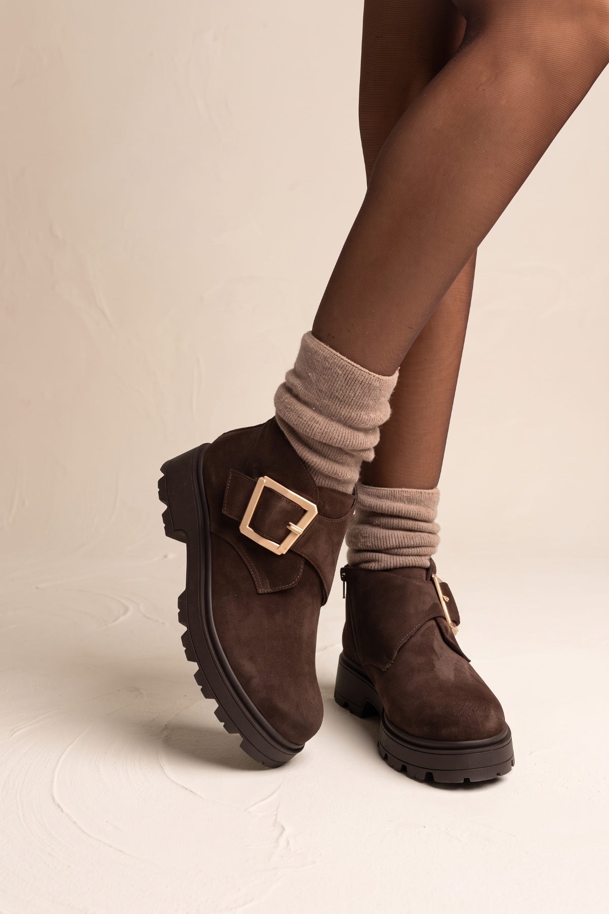 Model wearing brown suede ankle boots with chunky lug sole and gold buckle viewed from the front
