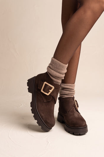 Model wearing brown suede ankle boots with chunky lug sole and gold buckle viewed from the front