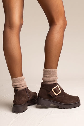 Model wearing brown suede chunky ankle boots with gold buckle and beige knit socks from the side