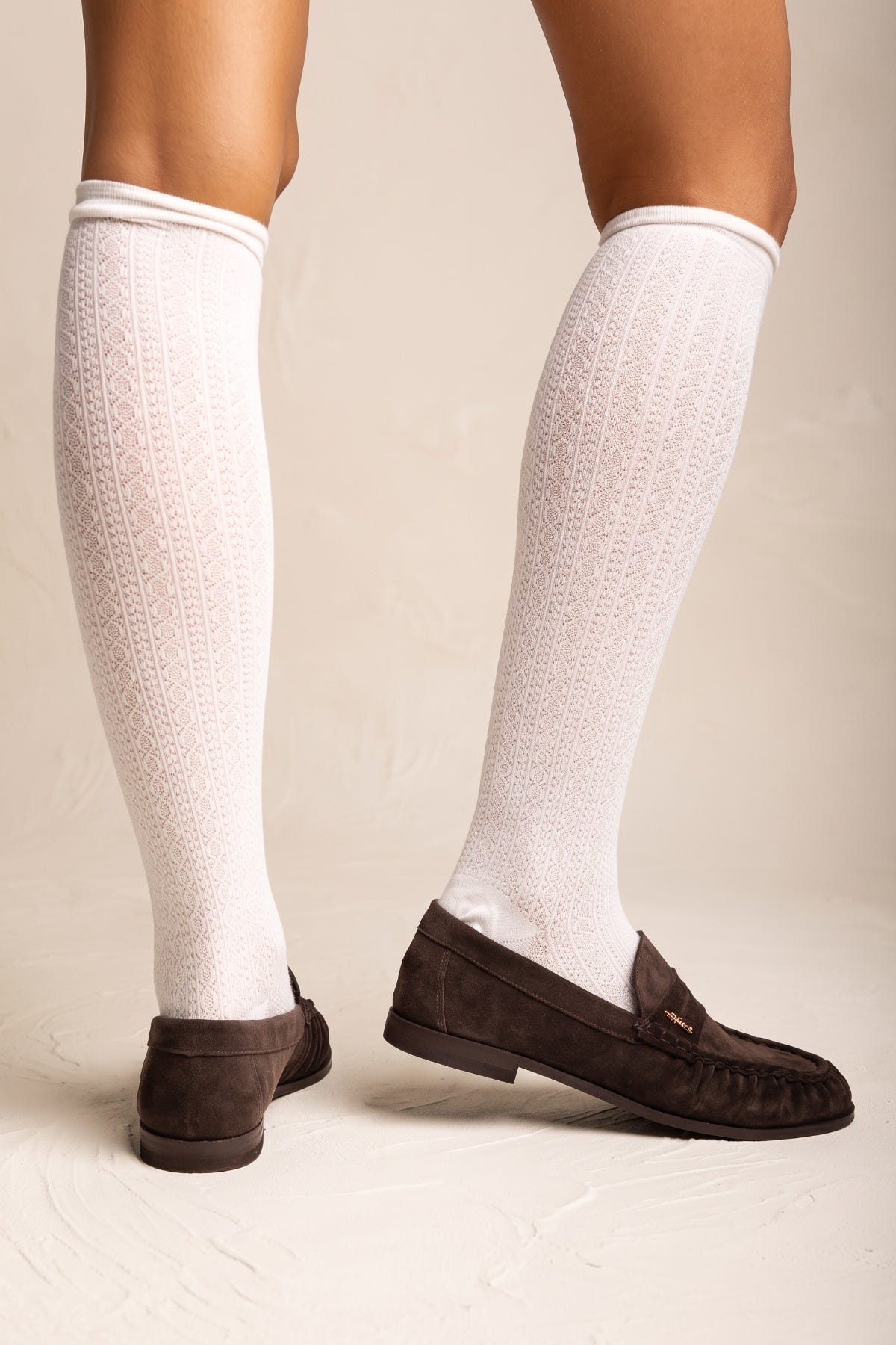 Brown suede flat loafers with pleated detail and moc stitching shown from the front with white socks