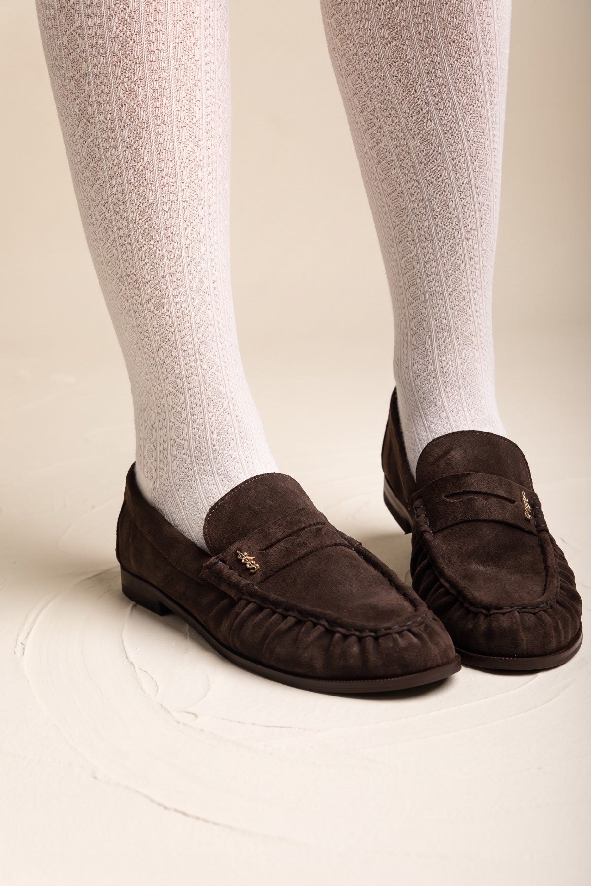 Brown suede penny loafers with pleated vamp worn with white knee-high ribbed socks in side view