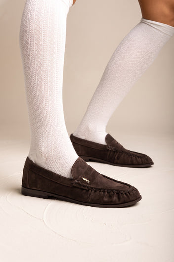 Brown suede flat loafers with pleated detail and small gold accent worn with white knee socks