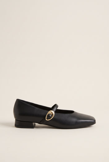 Black leather Mary Jane shoe with square toe, gold oval buckle strap and low block heel, side view on plain background