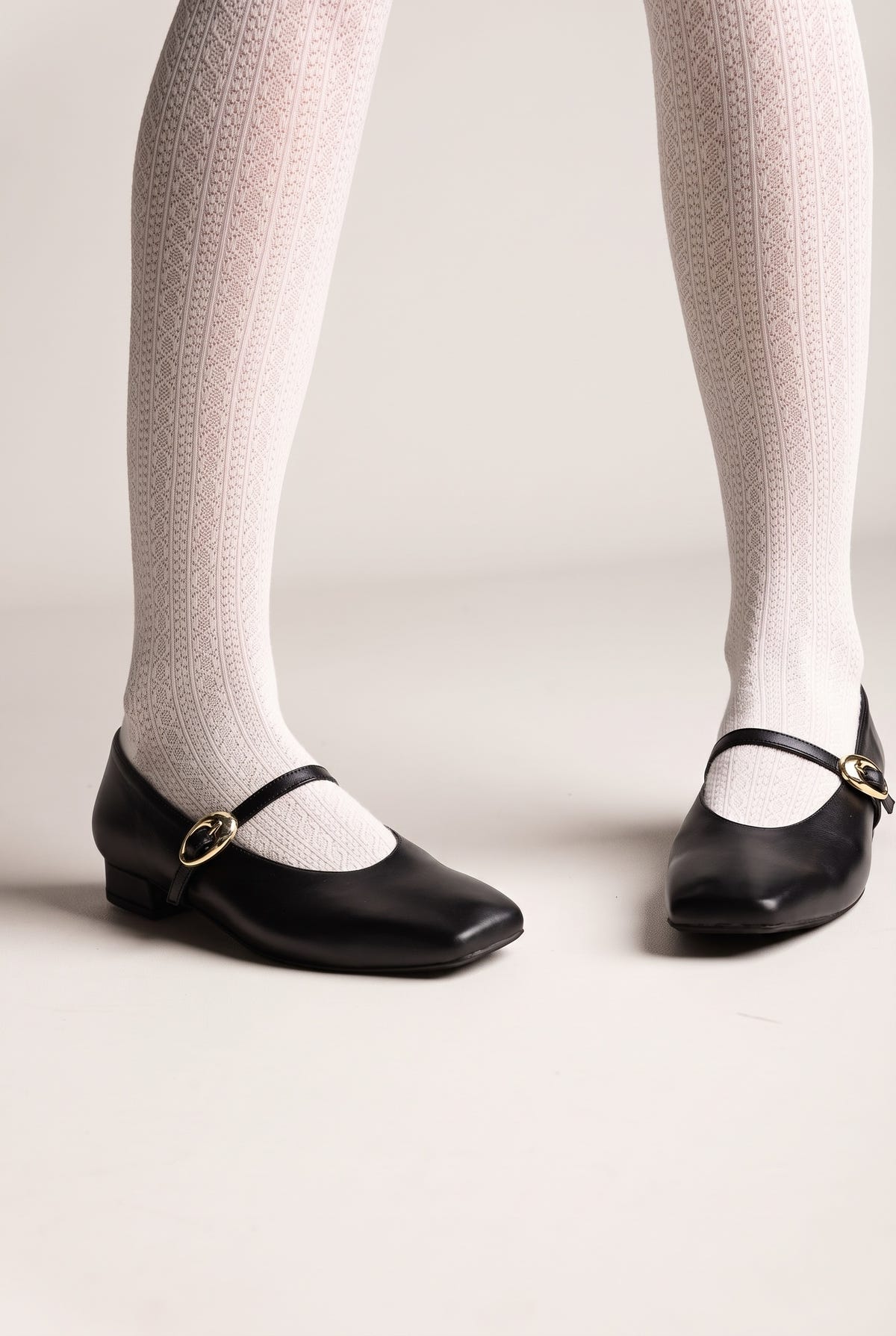 Black leather Mary Jane flats with square toe, ankle strap, gold buckle and low block heel, worn on model