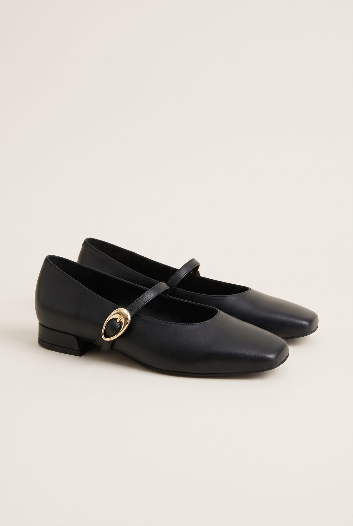 Pair of black leather Mary Jane shoes with square toes, gold buckle straps and low block heels, three-quarter view