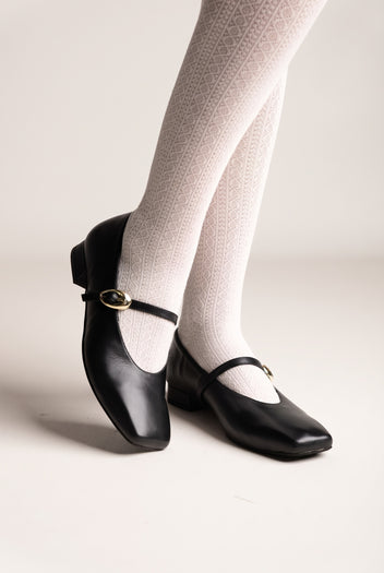 Black leather Mary Jane shoes with square toe, instep strap with gold buckle and low heel, worn on model, angled view