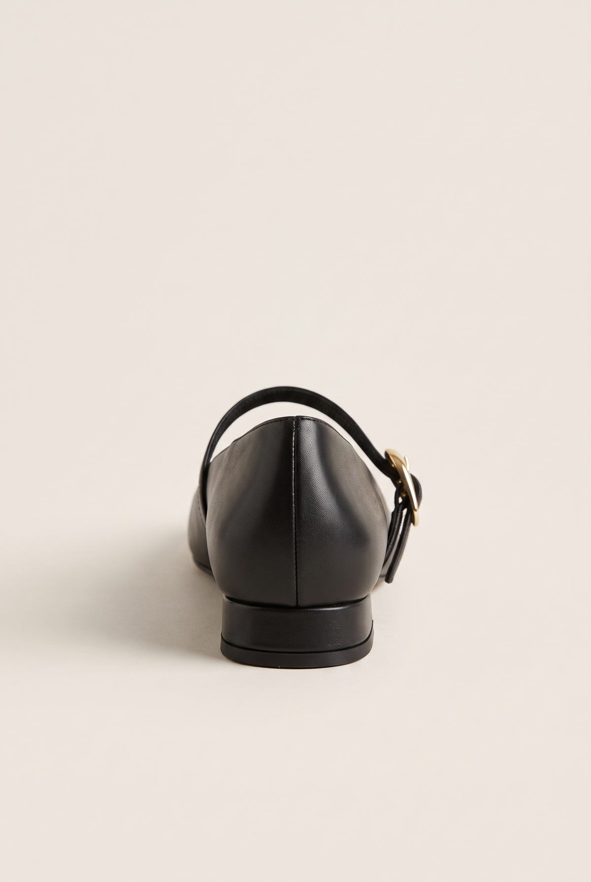 Back view of black leather Mary Jane shoe with low block heel, instep strap and gold buckle, on plain background