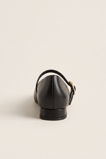 Back view of black leather Mary Jane shoe with low block heel, instep strap and gold buckle, on plain background