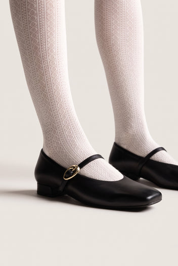 Black leather Mary Jane shoes with square toe, strap and gold oval buckle and low heel, worn on model, side view