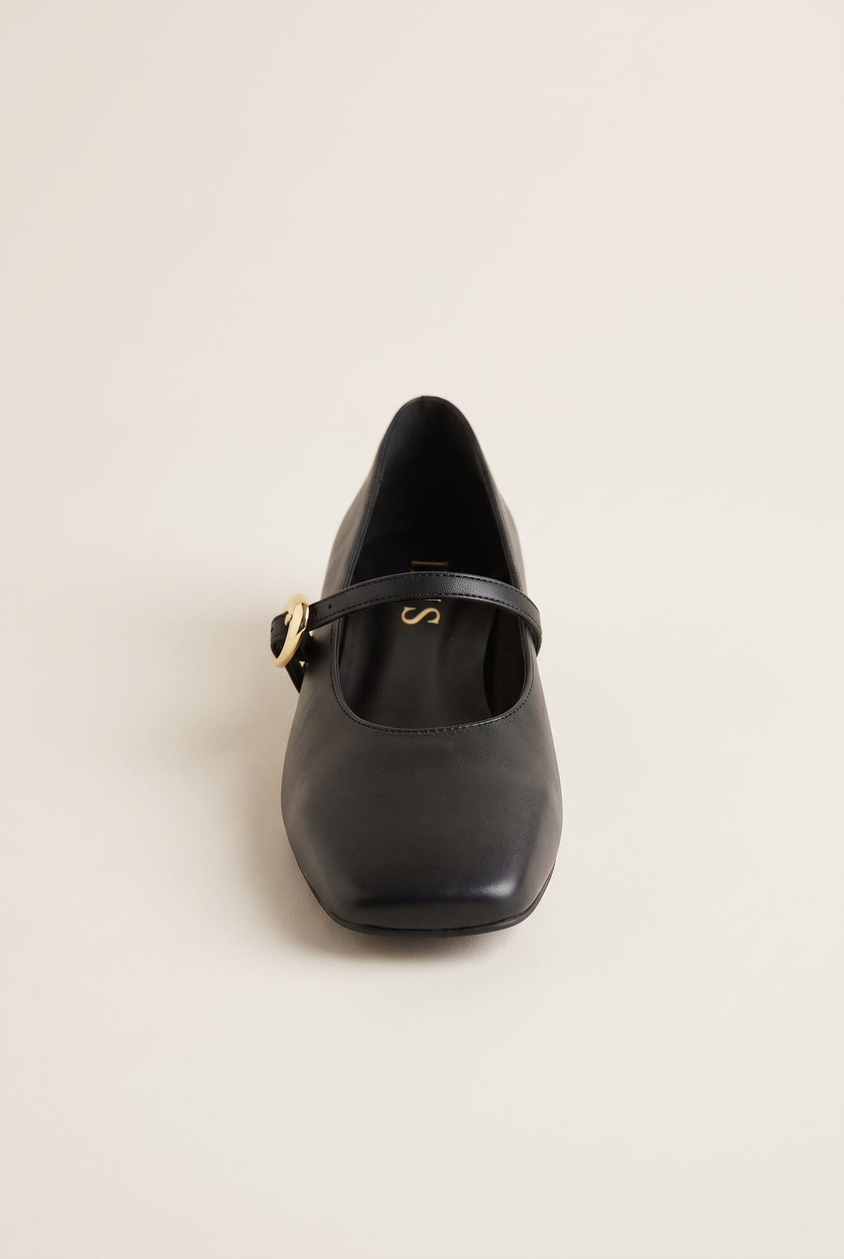 Front view of black leather Mary Jane shoe with square toe and strap with gold buckle, on plain background