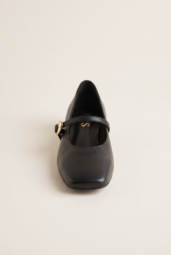 Front view of black leather Mary Jane shoe with square toe and strap with gold buckle, on plain background