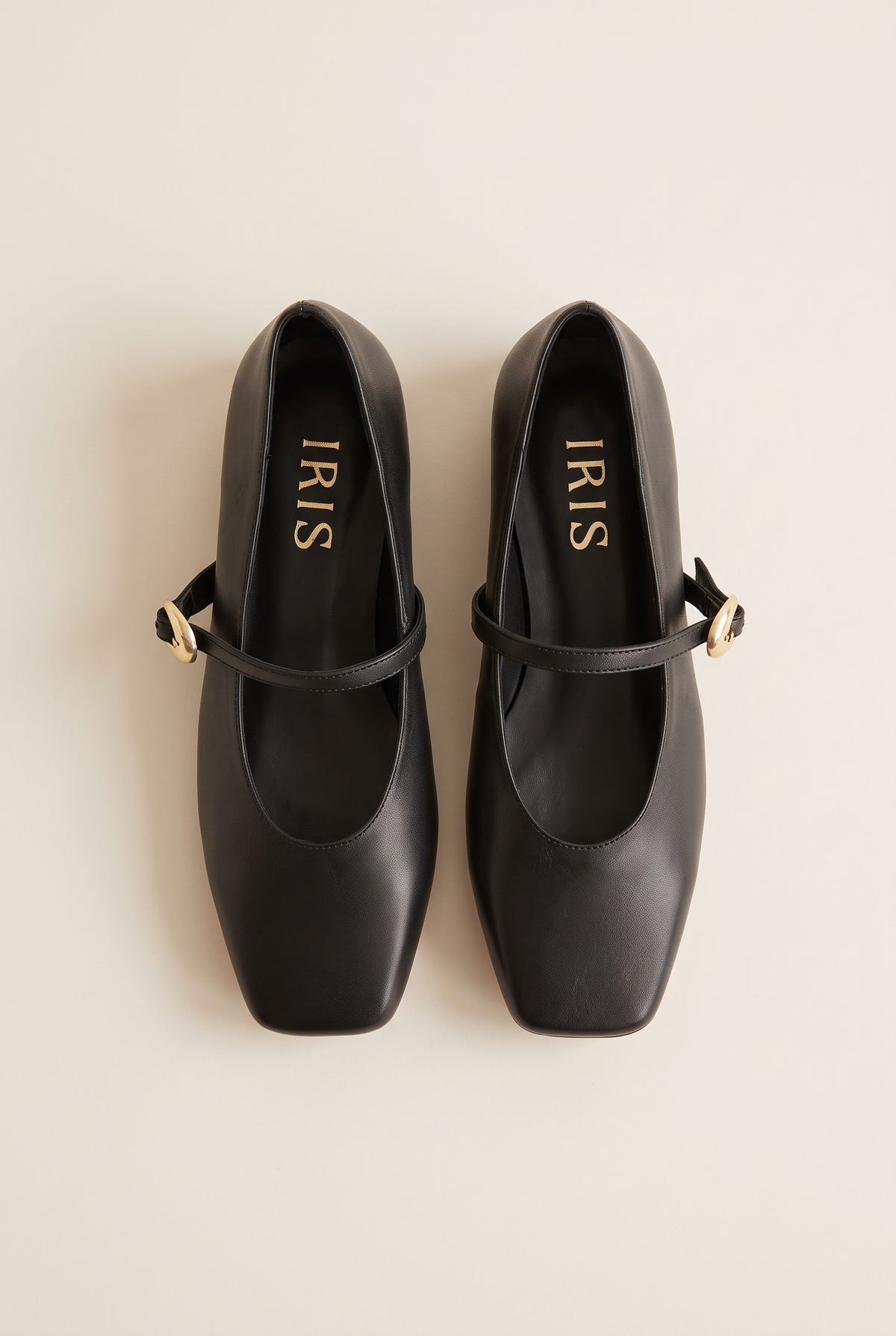 Top-down flat lay of a pair of black leather Mary Jane shoes with gold buckle straps and square toes