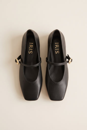 Top-down flat lay of a pair of black leather Mary Jane shoes with gold buckle straps and square toes