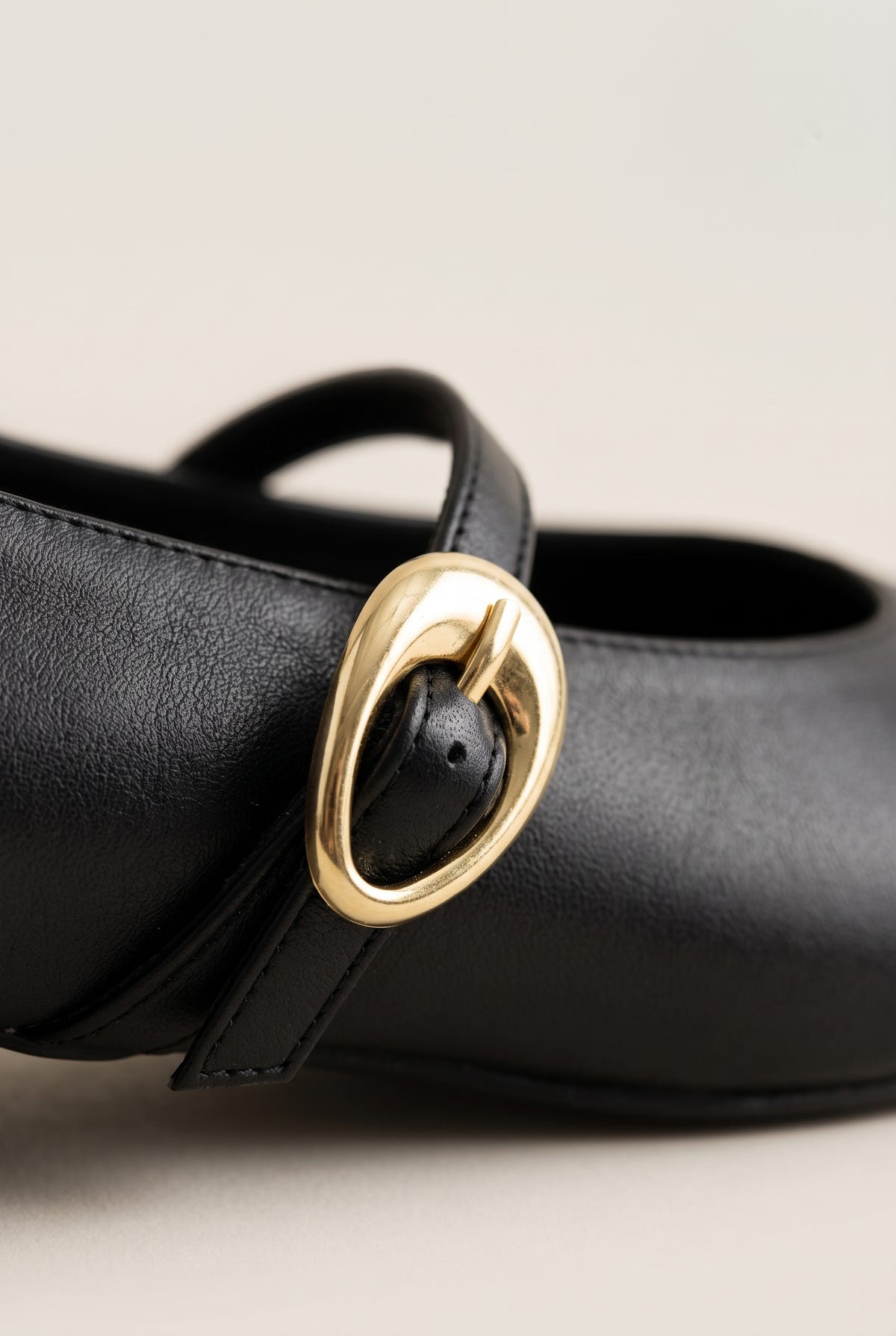 Close-up of black leather Mary Jane shoe with strap and oval gold buckle, textured smooth leather