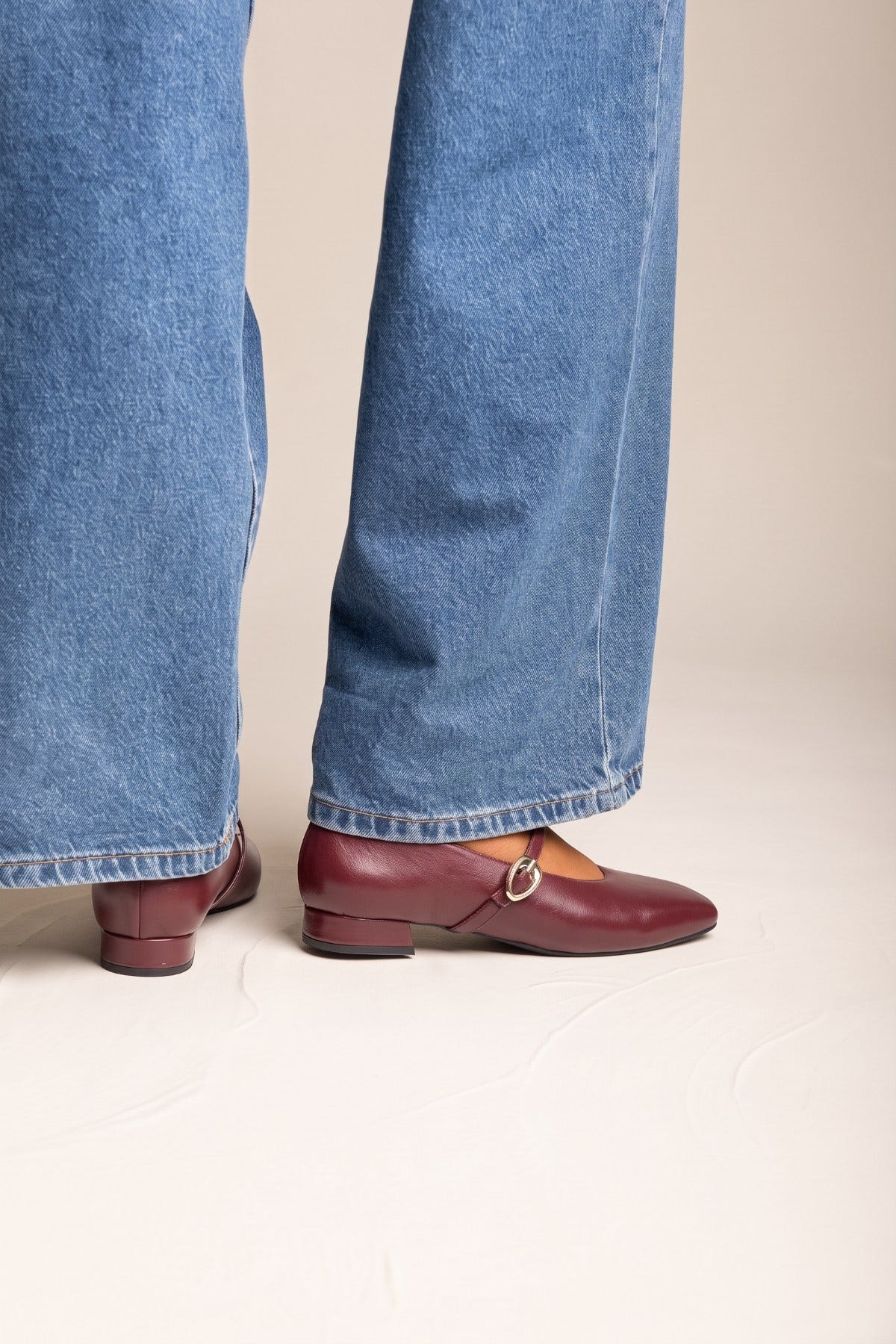 Pair of bordeaux matte square toe Mary Jane flats with ankle straps, worn with blue jeans
