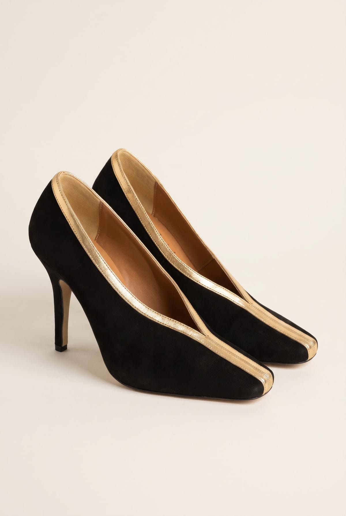 Pair of black suede pumps seen at an angle with gold metallic trim outlining the open vamp