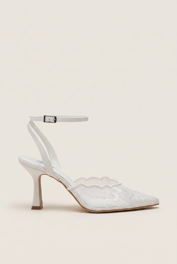 Side view of a white lace pump with a thin ankle strap, buckle closure and a slim stiletto heel
