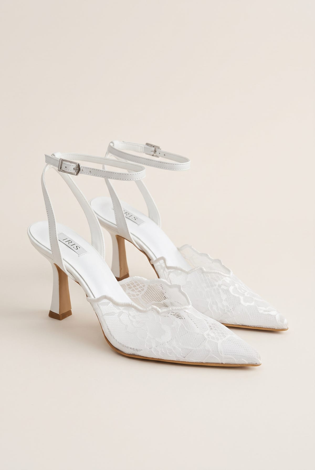 Pair of white lace pumps seen at an angle with thin ankle straps and scalloped lace panels on the vamp
