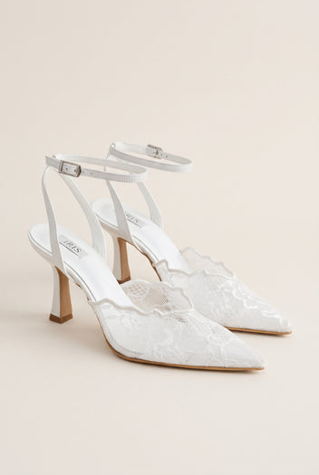 Pair of white lace pumps seen at an angle with thin ankle straps and scalloped lace panels on the vamp