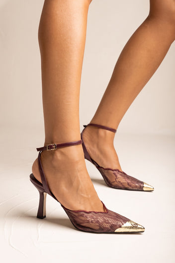 Model wearing bordeaux lace stiletto pumps with gold pointed toe caps and thin ankle straps