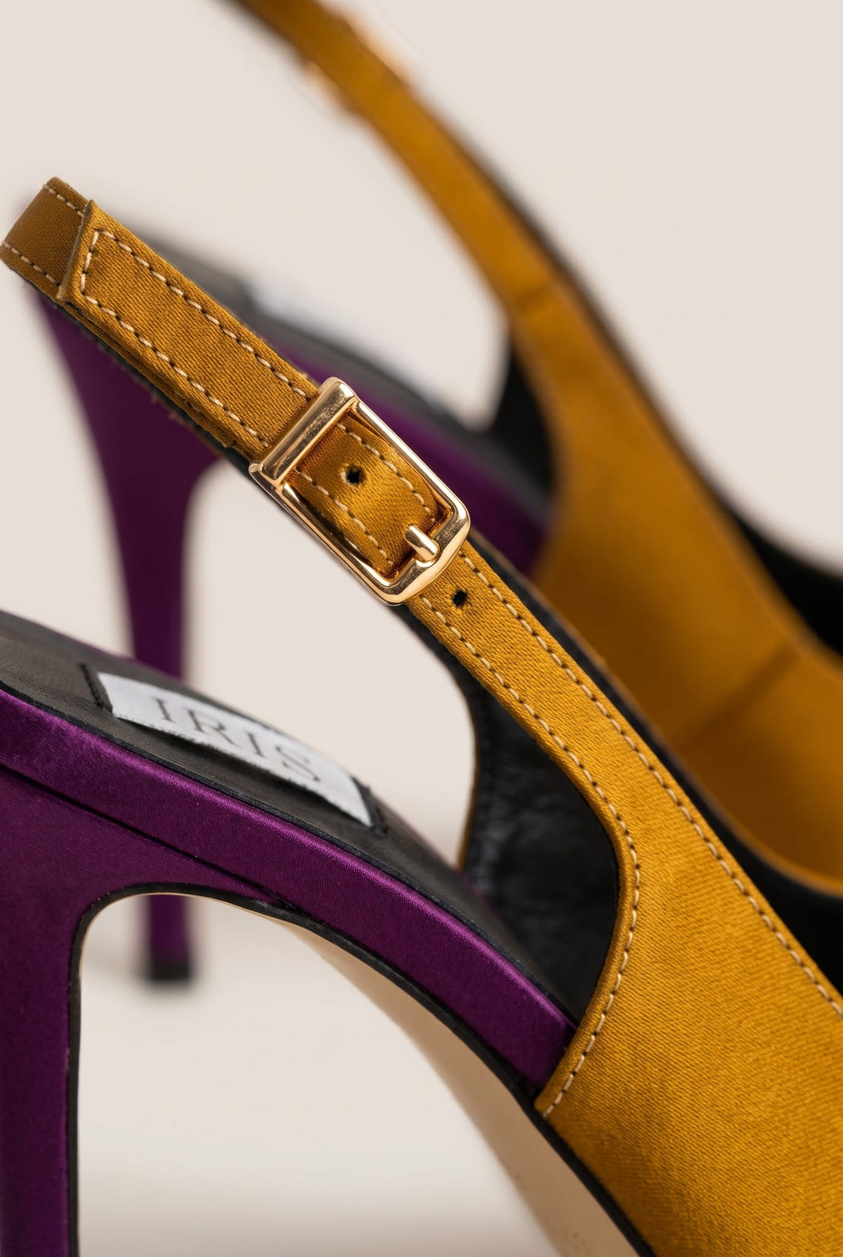 Close-up of an olive satin strap with a gold buckle beside a purple heel and dark insole