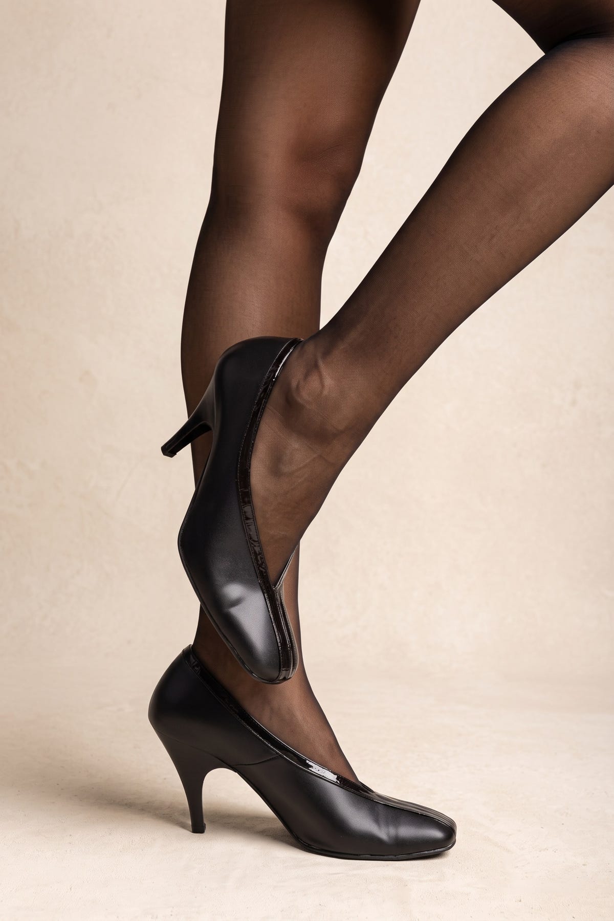 Black smooth leather pumps with a rounded toe, thin stiletto heel and glossy trim along the opening, on model