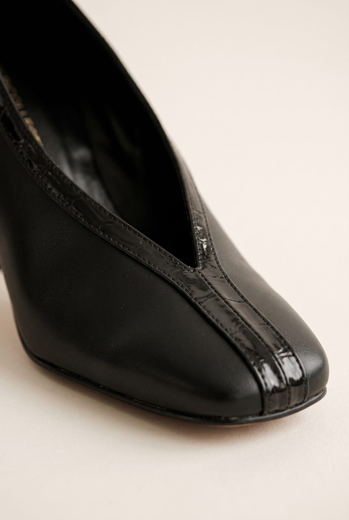 Close-up of black court shoe toe with V-shaped vamp cut and glossy croc-embossed trim over smooth leather