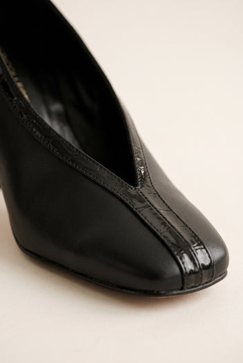 Close-up of black court shoe toe with V-shaped vamp cut and glossy croc-embossed trim over smooth leather