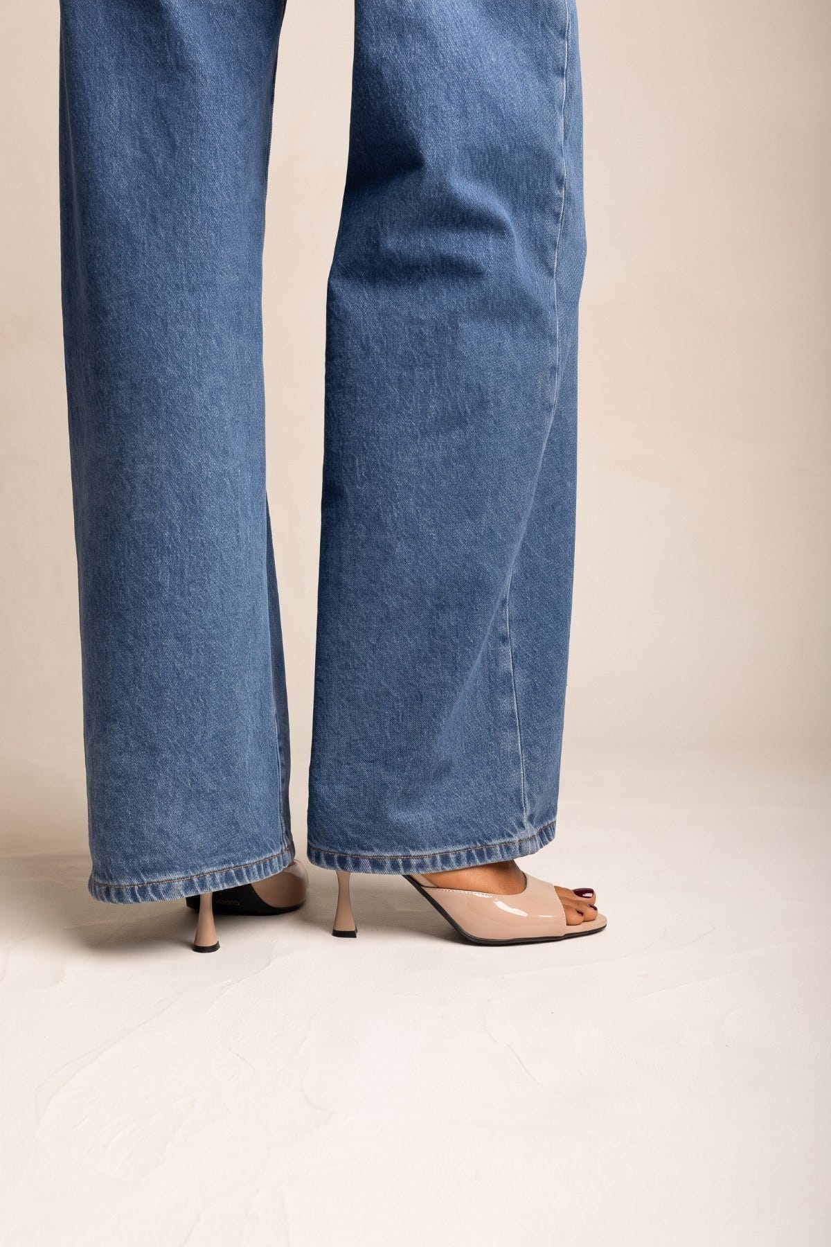 Nude patent stiletto mule with open toe and thin heel, pair worn with wide-leg blue jeans