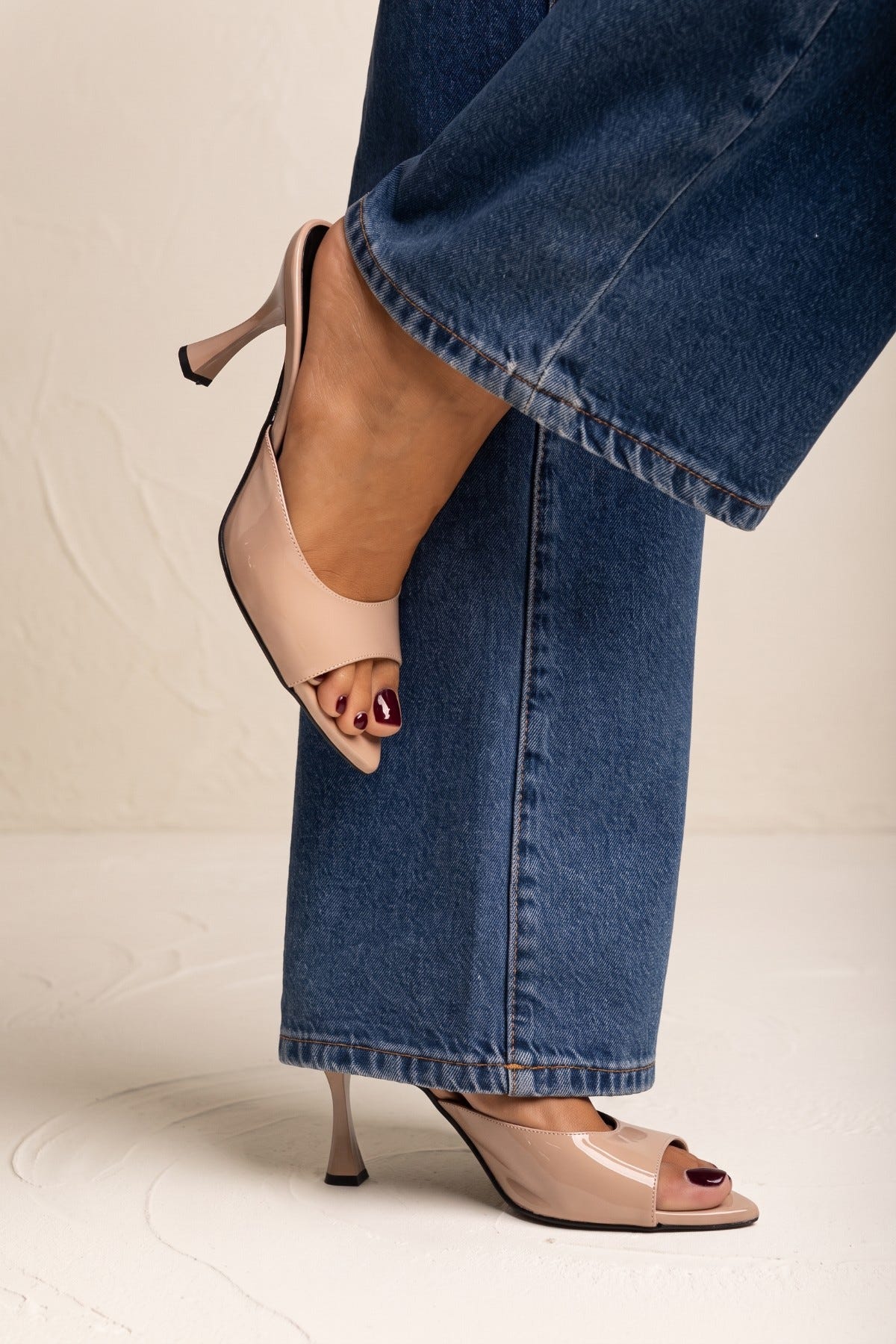 Nude patent stiletto mule with open square toe and slim heel, model legs in blue jeans