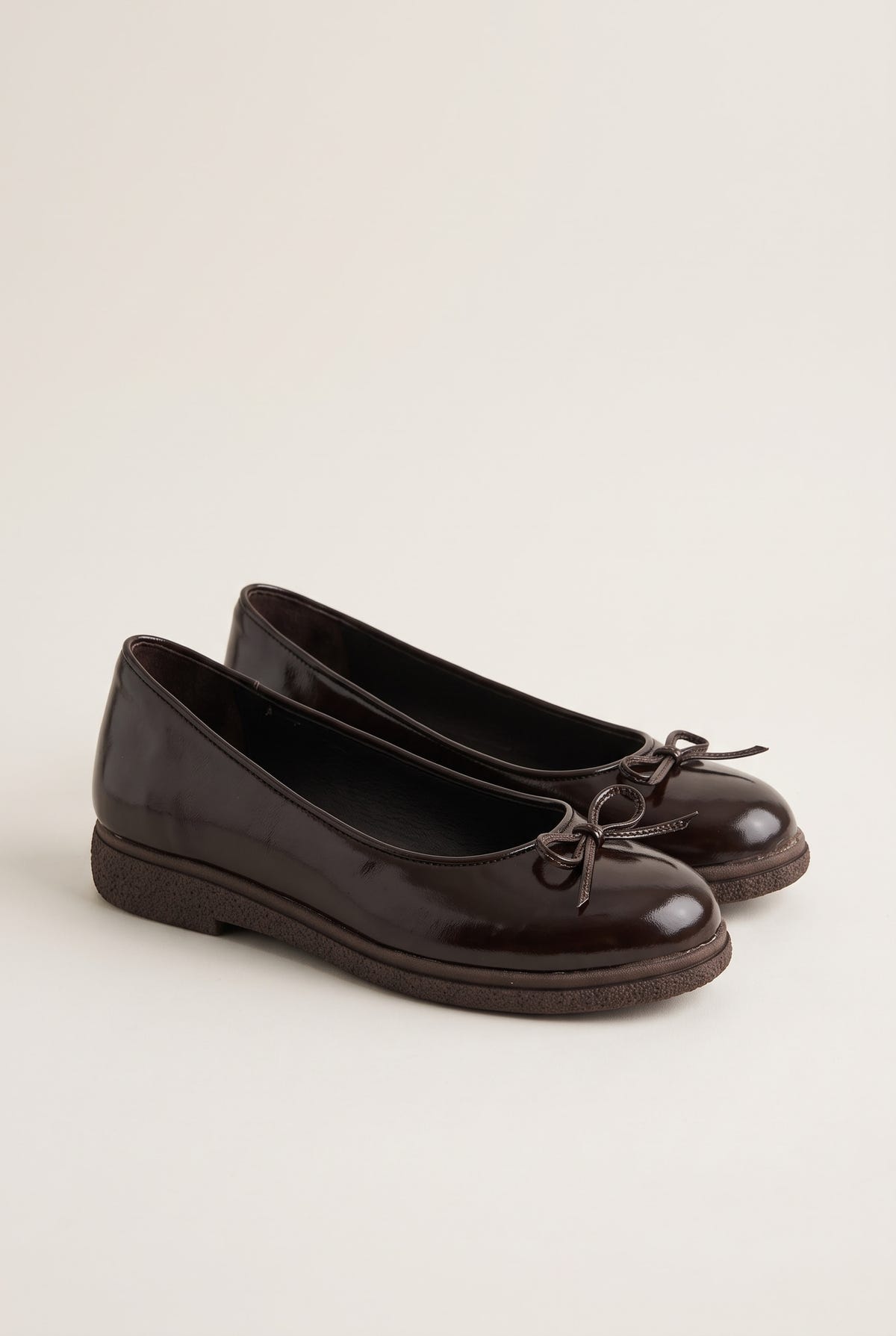 pair of glossy dark brown patent ballet flats angled to show the small bow and low rubber sole