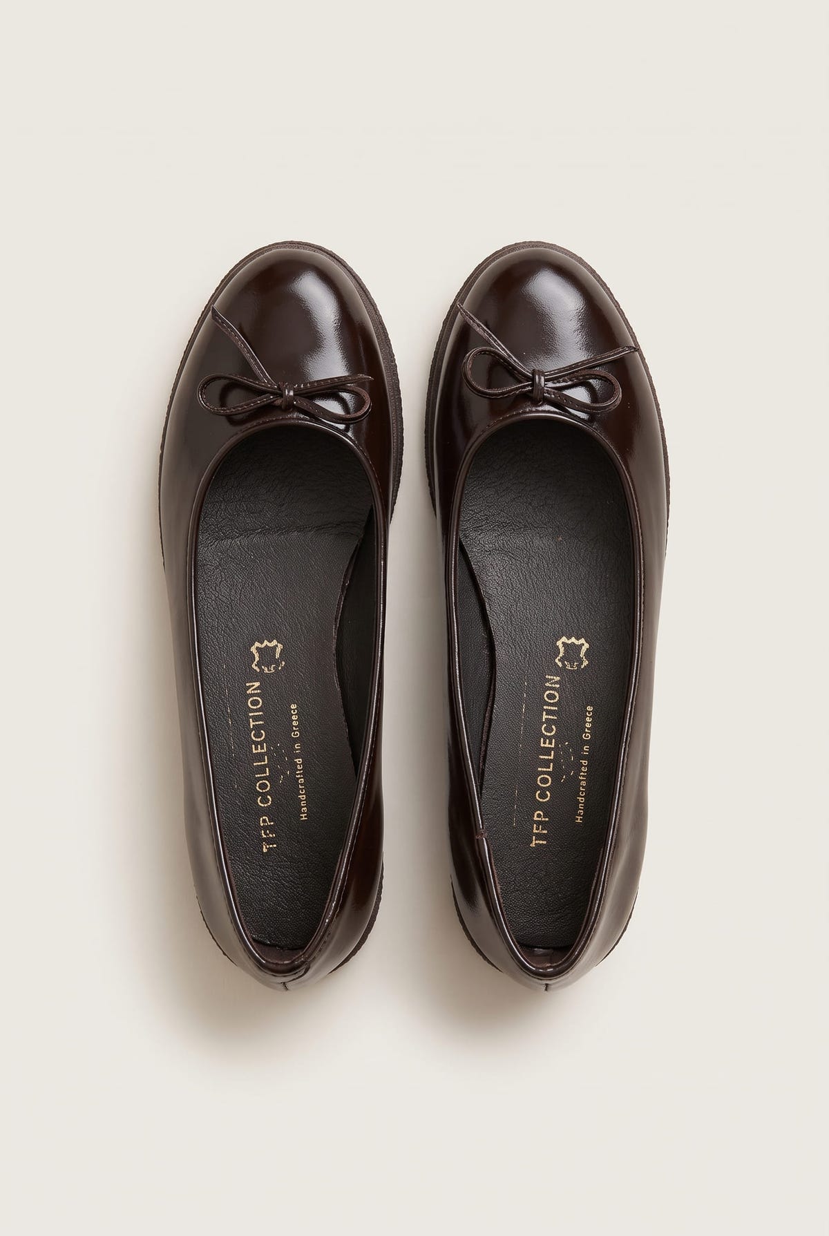 top view of a pair of glossy dark brown patent ballet flats with a small bow on the toes and insoles visible