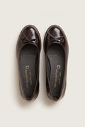 top view of a pair of glossy dark brown patent ballet flats with a small bow on the toes and insoles visible