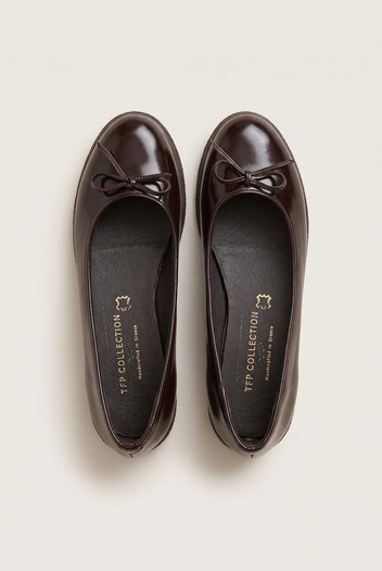 top view of a pair of glossy dark brown patent ballet flats with a small bow on the toes and insoles visible