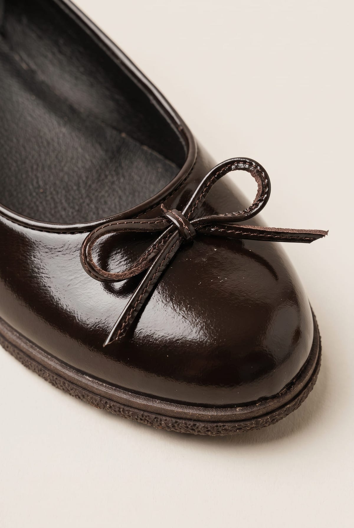 close-up of a glossy dark brown patent ballet flat toe with a thin bow detail and rounded cap toe