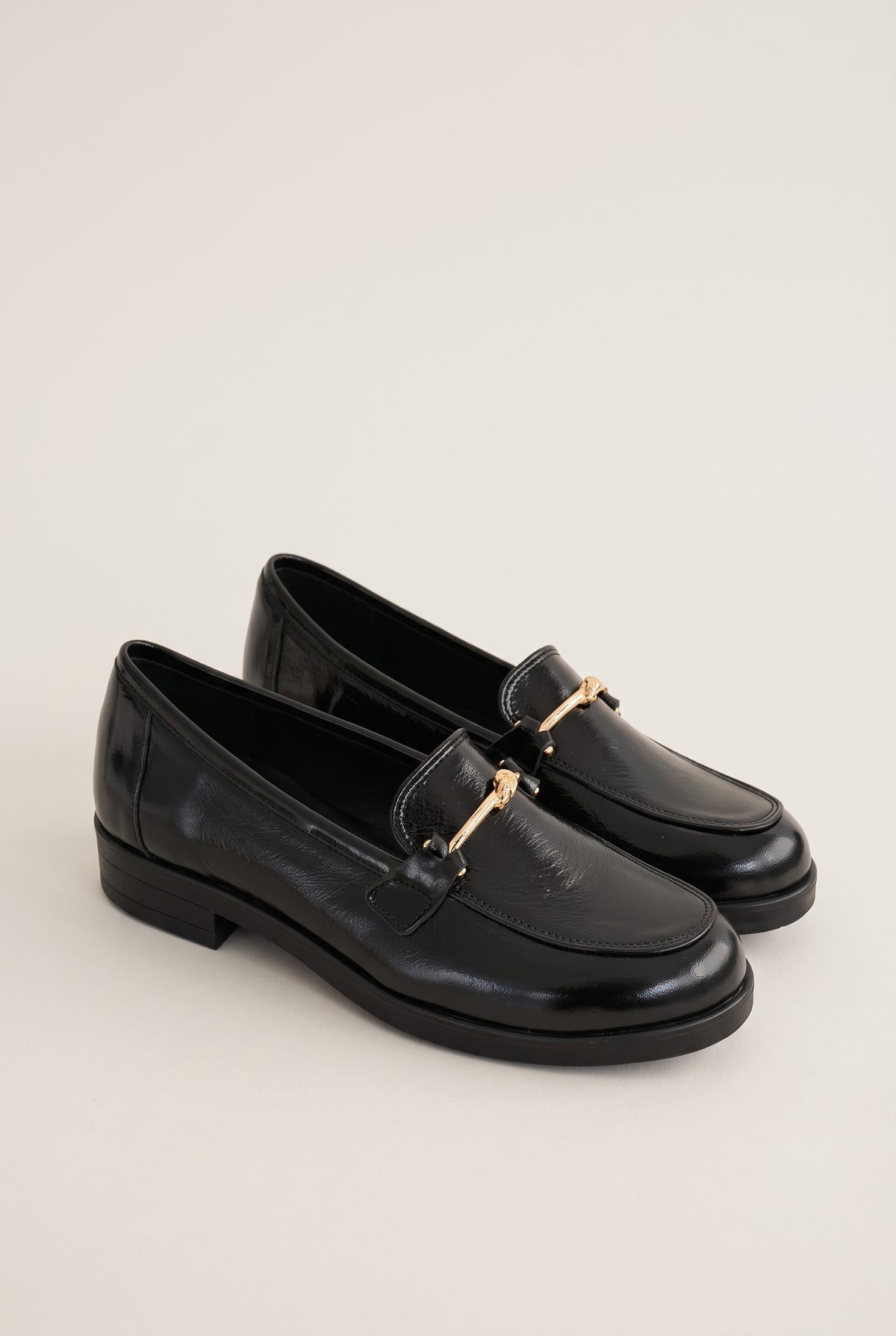 Pair of black patent horsebit loafers placed together in side view with a low flat heel