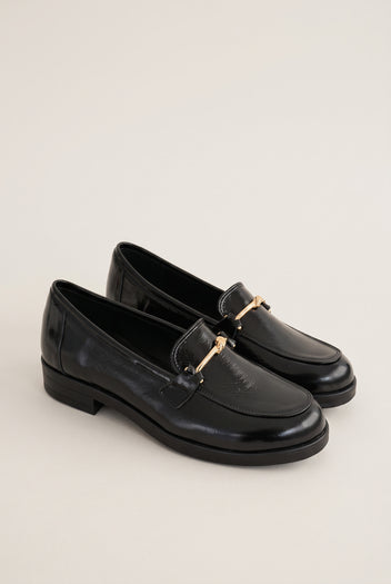 Pair of black patent horsebit loafers placed together in side view with a low flat heel