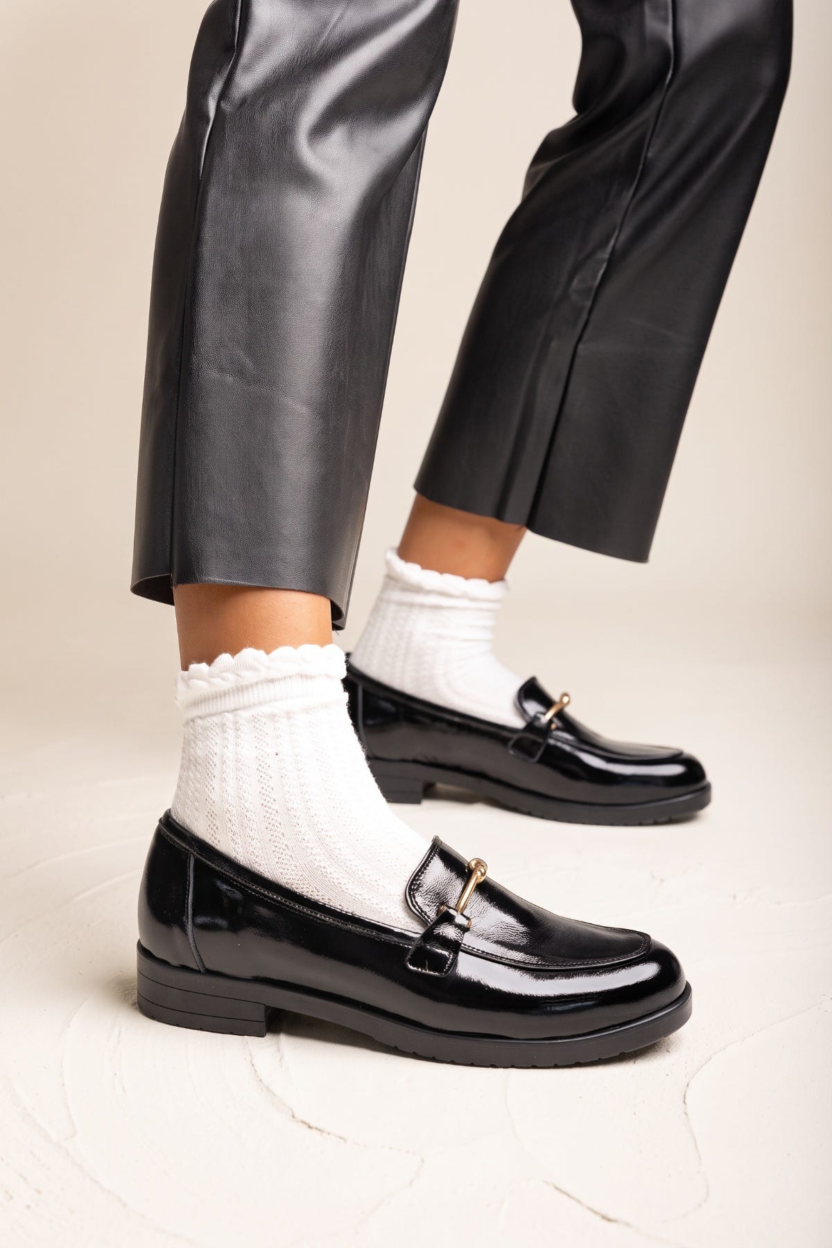 Model in black trousers wearing black patent horsebit loafers with white ruffled socks in side view