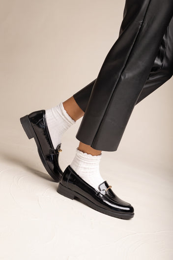 Model in black trousers and white ruffled socks stepping in black patent horsebit loafers in side view