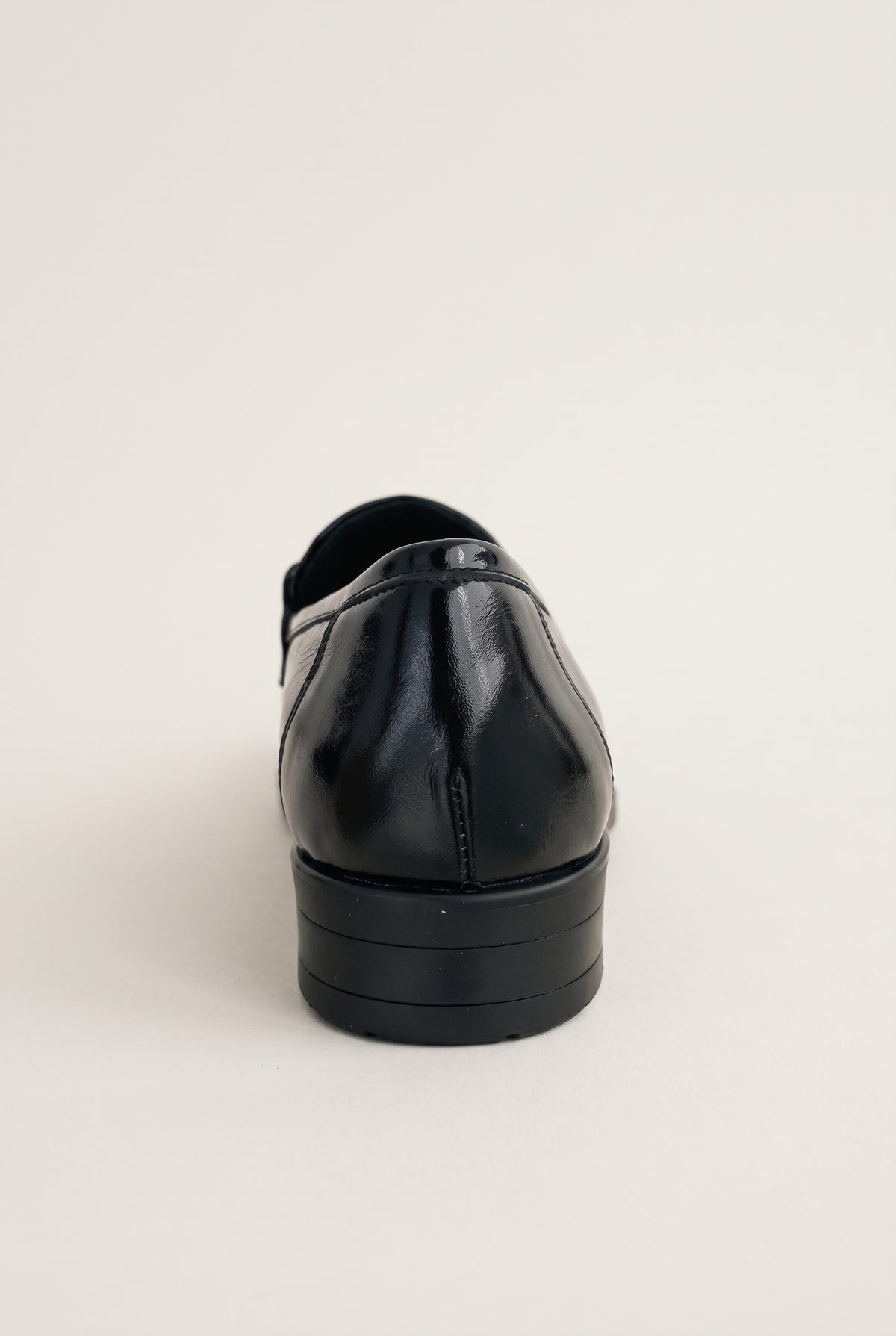 Back view of a black patent horsebit loafer showing the smooth heel counter and low flat sole