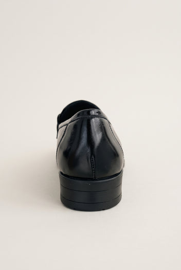Back view of a black patent horsebit loafer showing the smooth heel counter and low flat sole