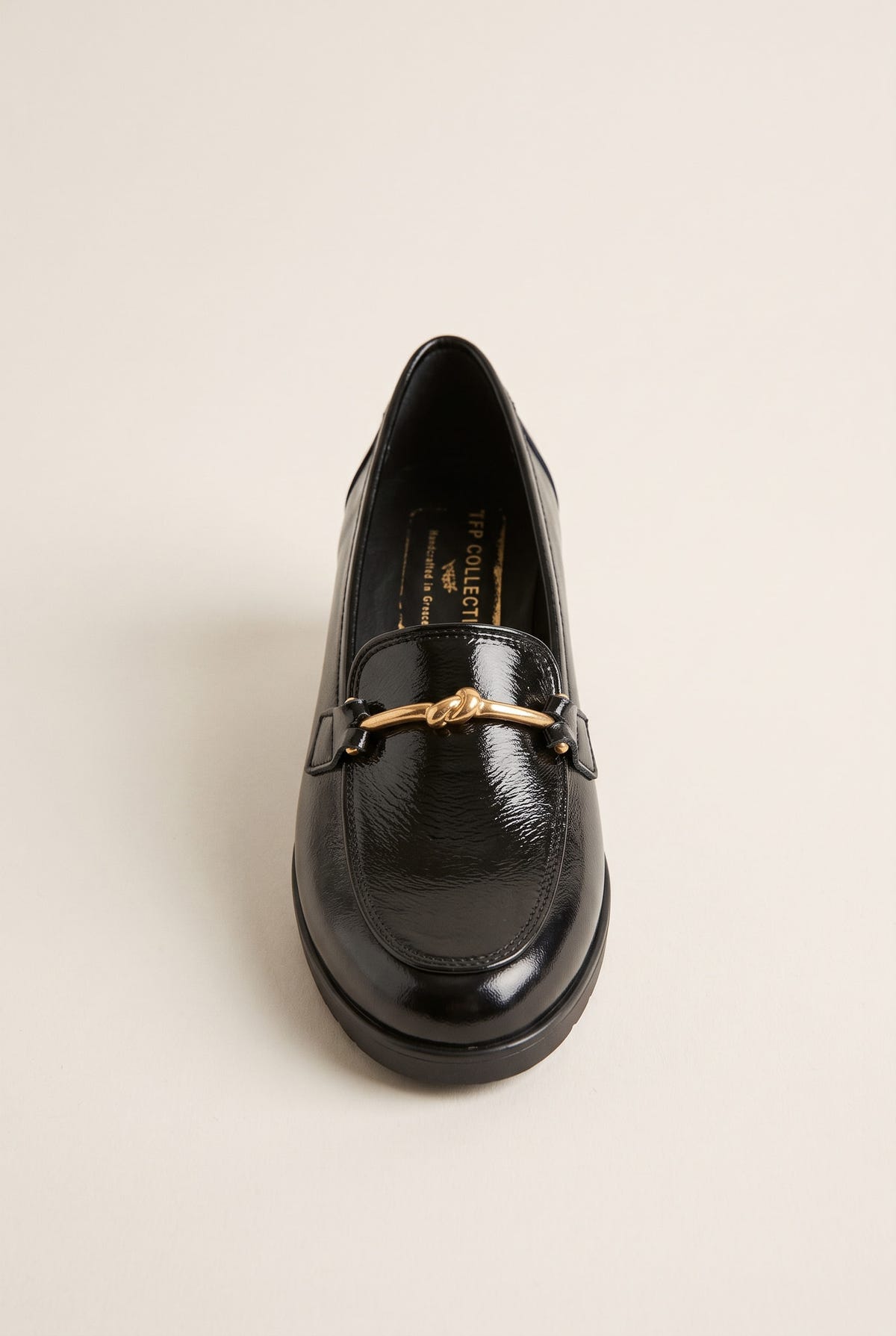 Front view of a black patent horsebit loafer with gold bar detail and rounded toe on a flat sole