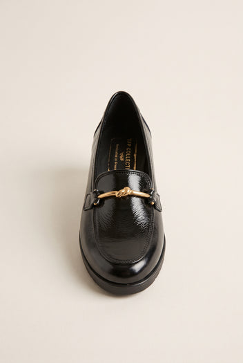 Front view of a black patent horsebit loafer with gold bar detail and rounded toe on a flat sole