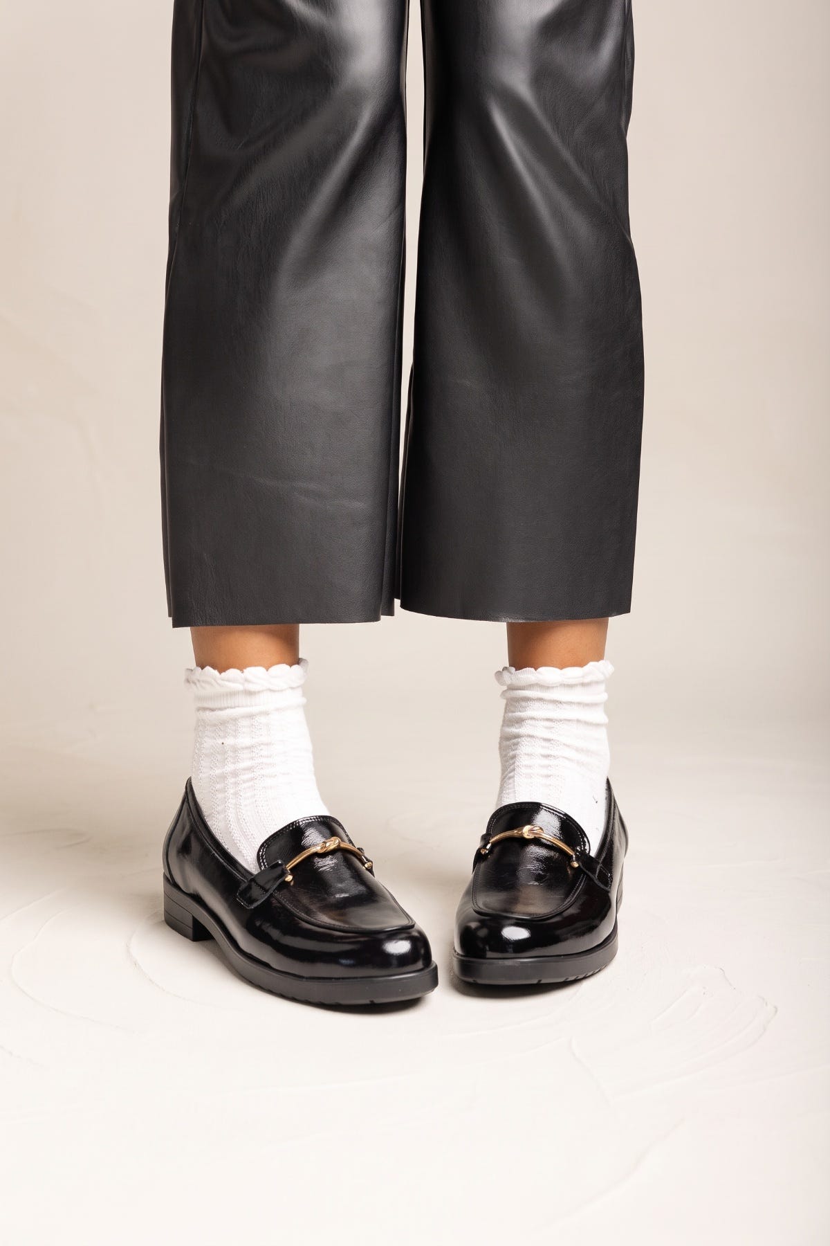 Model in black trousers and white ruffled socks standing in black patent horsebit loafers with feet apart