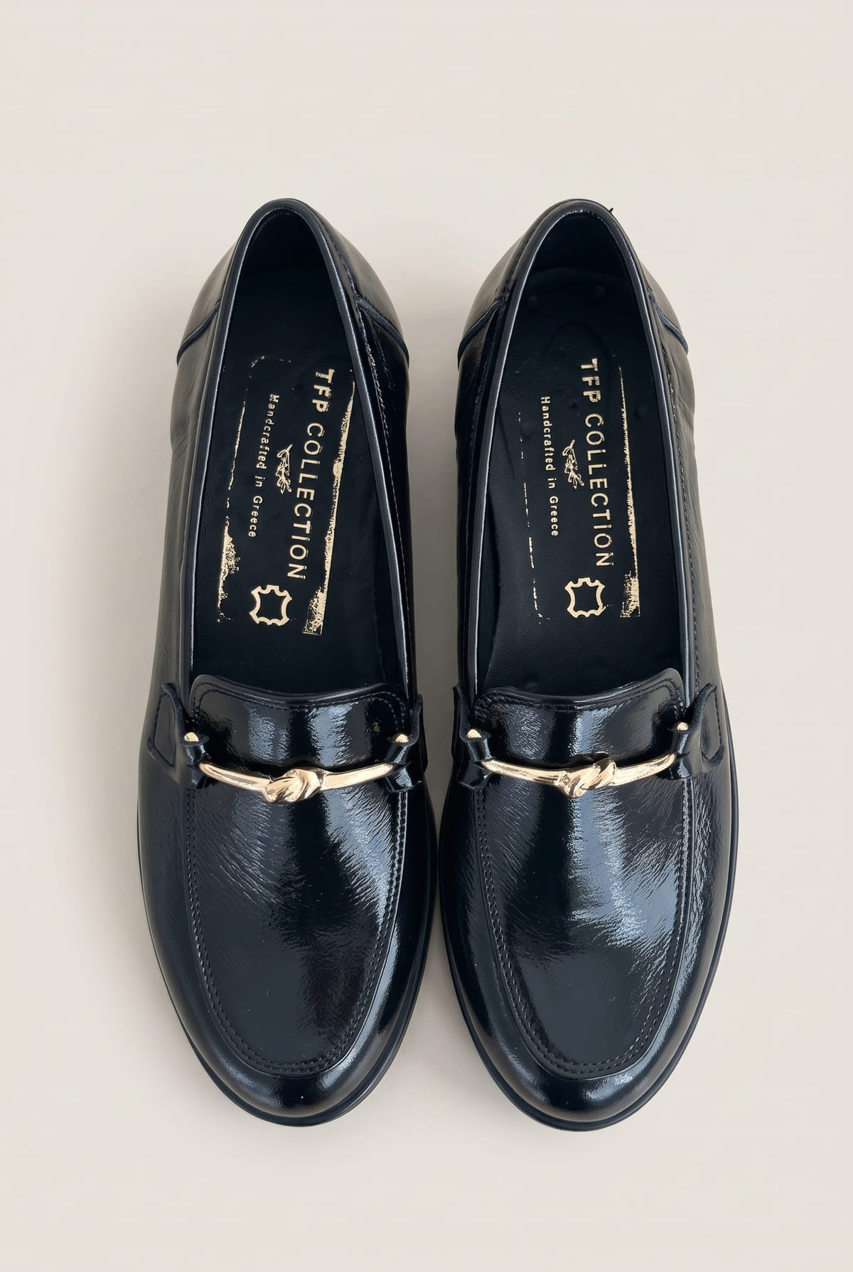 Top view of a pair of black patent horsebit loafers with gold bar detail and rounded toes