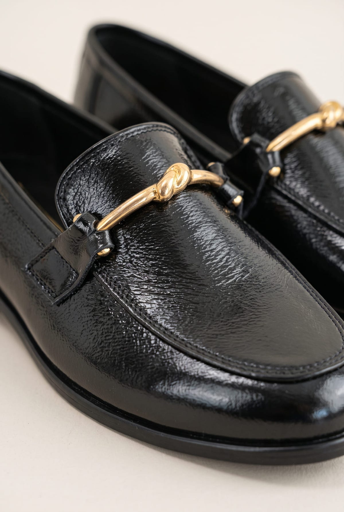 Close-up of a black patent horsebit loafer with gold bar detail and textured glossy leather upper
