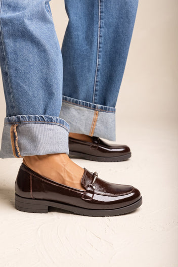 Model in cuffed blue jeans wearing brown patent horsebit loafers with a chunky dark sole standing view