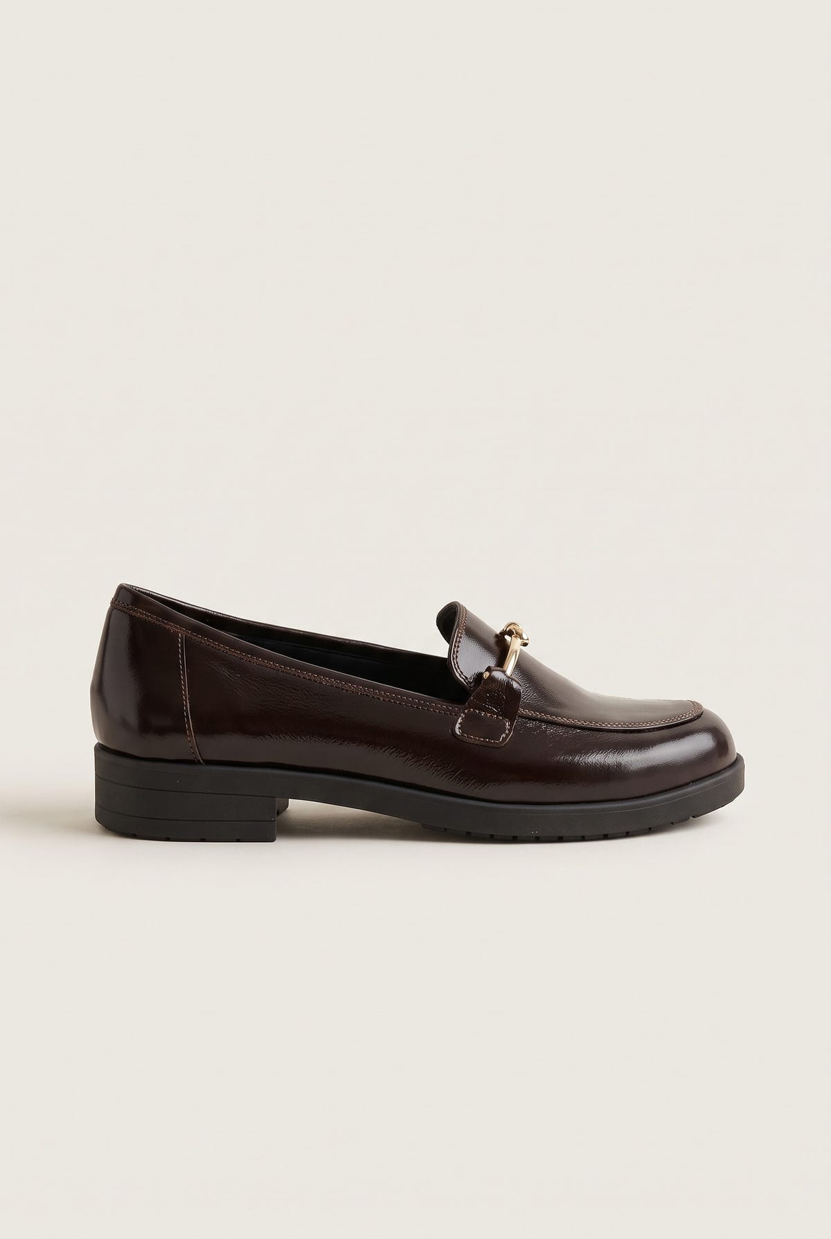 Side view of a single brown patent horsebit loafer with a gold metal bit and low block heel on a dark sole