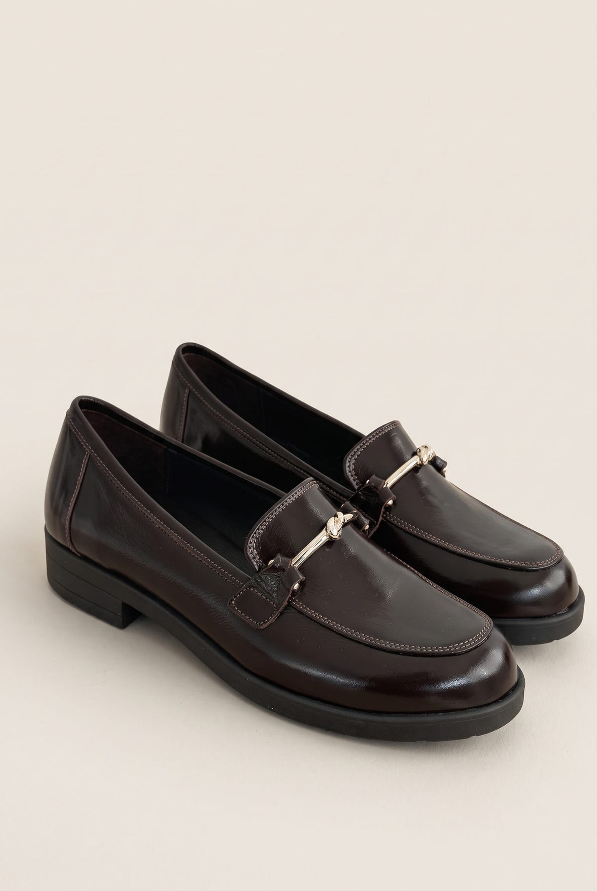 Angled view of a pair of brown patent horsebit loafers placed side by side showing dark rubber soles