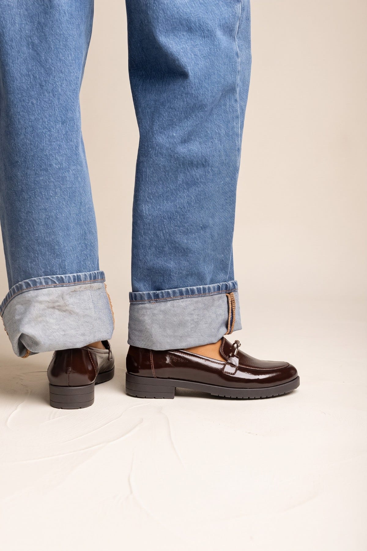 Model in cuffed jeans stepping forward in brown patent horsebit loafers with gold bit and chunky sole